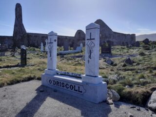 a white marble gravestone with the name O'Driscoll sits in the foreground, with the abbey ruins in the background