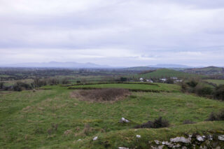 a view of the surrounding landscape, with houses visible in the near distance, and mountains just visible in the far distance, obscured slightly by mist and fog