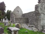 The exterior walls of the church stand roofless along the edge of a graveyard