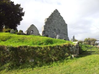 View of the top of the remaining walls of Aghowle church visible behind a small mound in the foreground of the image