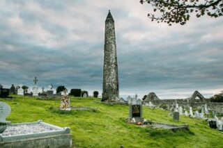 the round tower pierces the cloudy sky, its top pointed and cone-like.