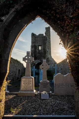 a view of the tower of the church, through an arched window, with gravestones in the foreground of the view.