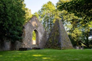 an arched section of the church of the abbey, with a glassless window in the centre, and a 3D triangular stone feature beside it.