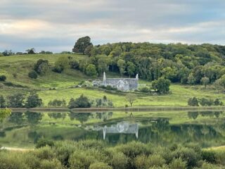 the remaining stone ruins of the abbey with a forest behind it, and the lake in front of it, in which it is reflected.