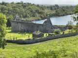 a view overlooking the abbey from a distance, with the lake still and peaceful in front of the ruins.