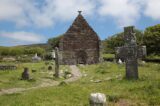 a small, dark stoned church, standing amongst the crosses, and backdropped by the mountains and blue sky