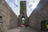 internal view of the inner walls of the abbey. Two women walk the grounds, and the tower of the church looms tall into the sky.