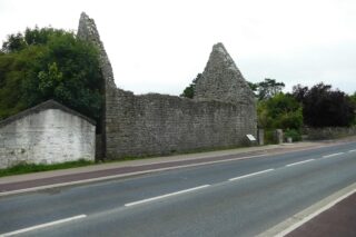 a long rectangular shaped church, now roofless, stands near the side of the road.