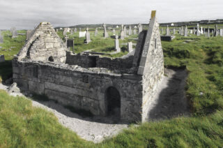 roofless church in the foreground, with numerous graves in the field behind it