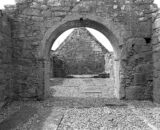 black and white photo of the interior ruins of a church. looking from one courtyard, through an arch into the other courtyard