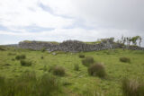 a view of the remains of the stone fort in a field, backdropped by the cloudy sky