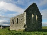 a view of the roofless remains of the church, the front and one side wall still intact.