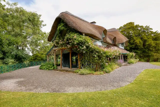 a thatched roof cottage with flowers and vines growing all around the front of the building