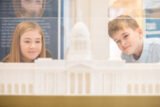 two children looking through a glass case at a model of the custom house