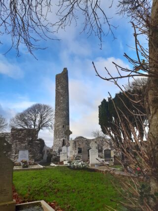 a round tower surrounded by graves, and backdropped by the blue sky