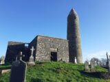 a round tower and a church situated within the cemetery, backdropped by the clear blue sky.