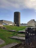 view of a small, short round tower, without a top, standing among graves.