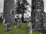 view of the bottom halves of the round tower and church, which are facing each other, within the cemetery.