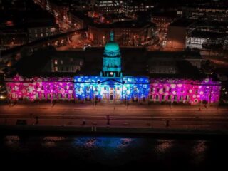 the custom house building lit up in pink and blue, with snowflake decorations on the front exterior, for Christmas