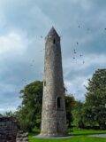 the round tower piercing the darkening grey sky, with birds flying around the top of the tower.