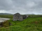 a roofless church building within the grass. The mountains are in the background, with the beach to the left.