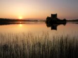 The sunset turning the water orange, and shadowing the castle ruins