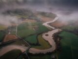 an aerial view of the abbey within the surrounding field landscape, and the river flowing nearby