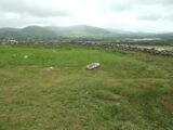 a horizontal ogham stone in the grass, with a low stone wall surrounding it, and the mountains in the background.