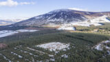 aerial view of the ringfort covered in snow, surrounded by the woods. A snow-covered mountain is in the background.