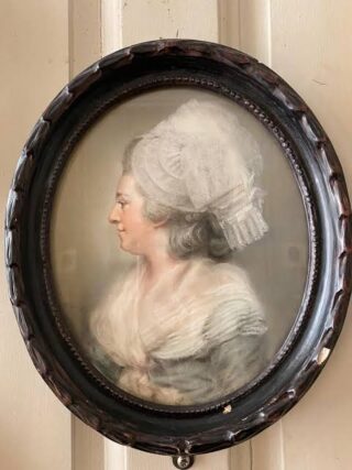 a portrait painting in an oval black frame of a woman, hanging on the wall