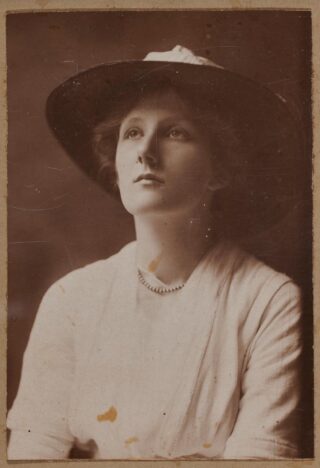 black and white image of a woman sitting looking at something off camera, wearing a hat