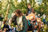 Actors dressed in medieval clothes are on horses.
