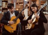 A man and a woman sit and play guitar