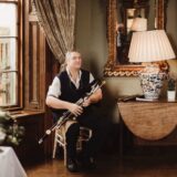 A man sits with 18th century pipes resting on his knee