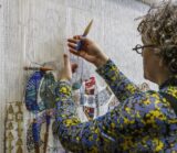 A woman hanging and working on a piece of cloth art on a wall.