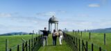 3 people walk toward a narrow open temple in the middle of an open field, and the blue sky as the backdrop