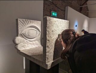 a woman looks intently at a carving depicting an eye