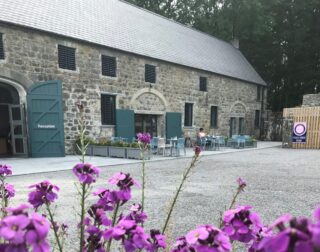 Exterior distant view of Protumna Castle Tearoom viewed through some purple flowers.