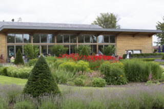 Exterior view of the Tea Pavillion in the Walled Garden at Oldbrige. We can see a beautiful bed of flowers with customers dining Al Fresco with the pavillion in the background.