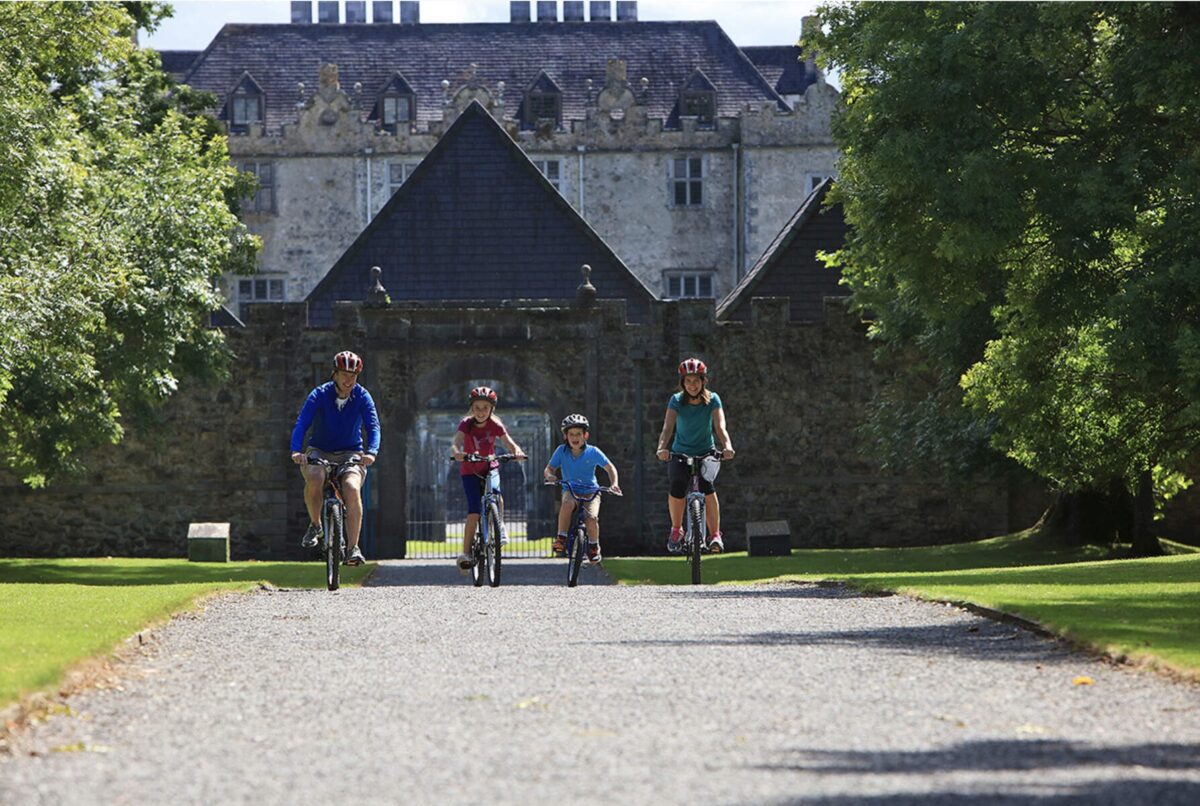 a family of four cycle down the gravel path, with the castle behind them