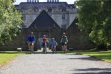 a family of four cycle down the gravel path, with the castle behind them