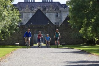 a family of four cycle down the gravel path, with the castle behind them