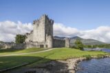 Exterior view of Ross Castleunder a pale blue sky with the river to the left and mountains in the background.