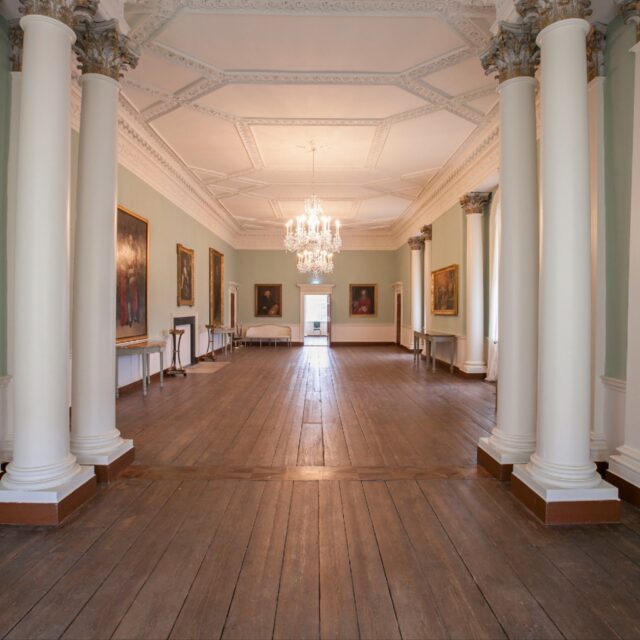 View of Hallway in Rathfarnham Castle which shows pillars,walls with pictures and a splendid chandelier