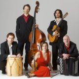 Four men and a women dressed in suits and a red dress pose with instruments.