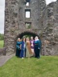 People stand outside an old Abbey dressed in 12th Century clothing.