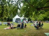 A park with 2 Gazebos lots of people seated on chairs and some on the grass