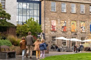 A family walk towards a cafe with al Fresco diners in sight outside the Silk Road Cafe in the grounds of Dublin Castle