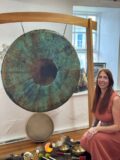A lady sits in front of a gong