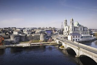 an aerial view of the castle beside the water, with a church across the bridge on the opposite side